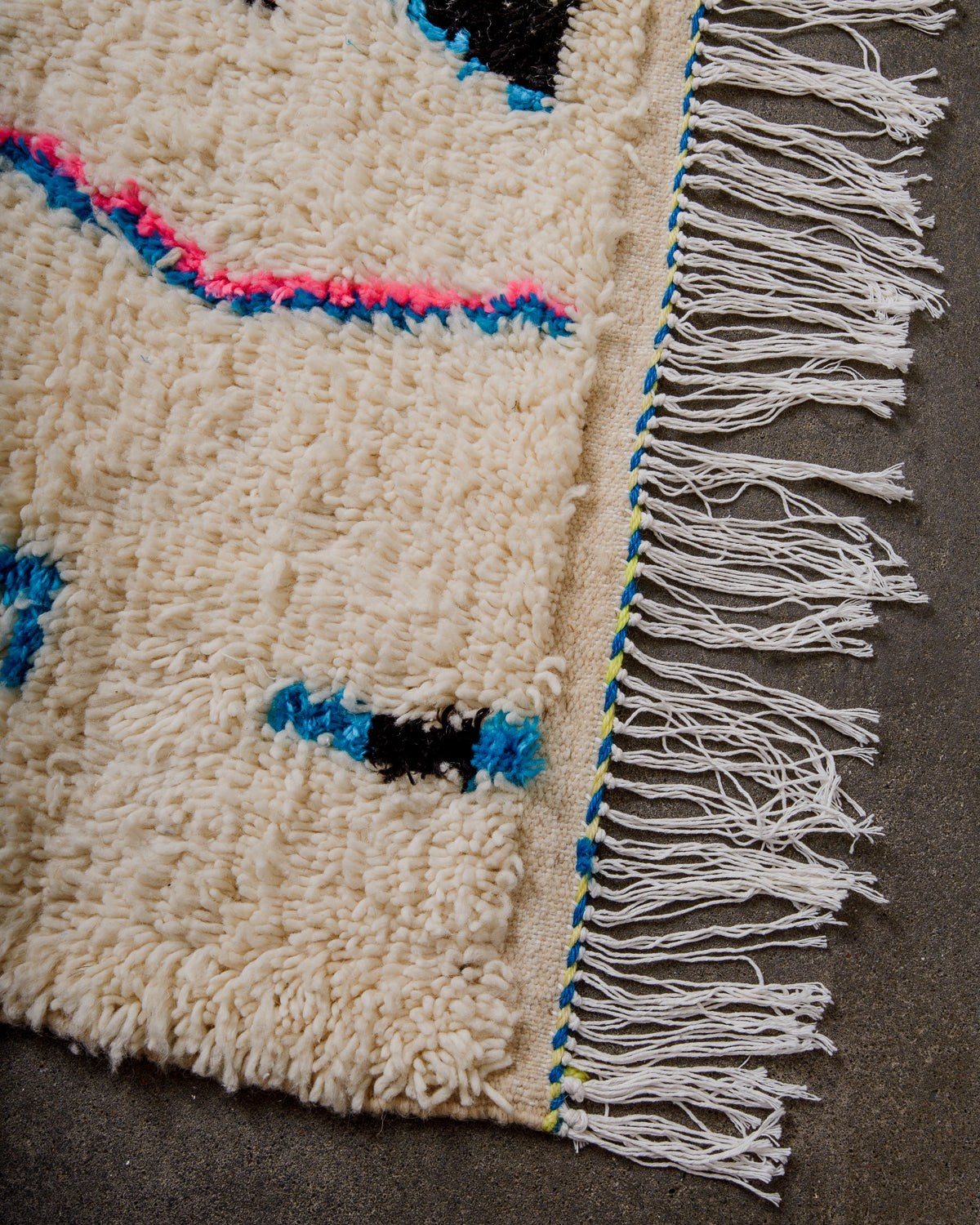 Corner of cream Azilal rug with a tightly woven edge and white cotton tassels across the top.
